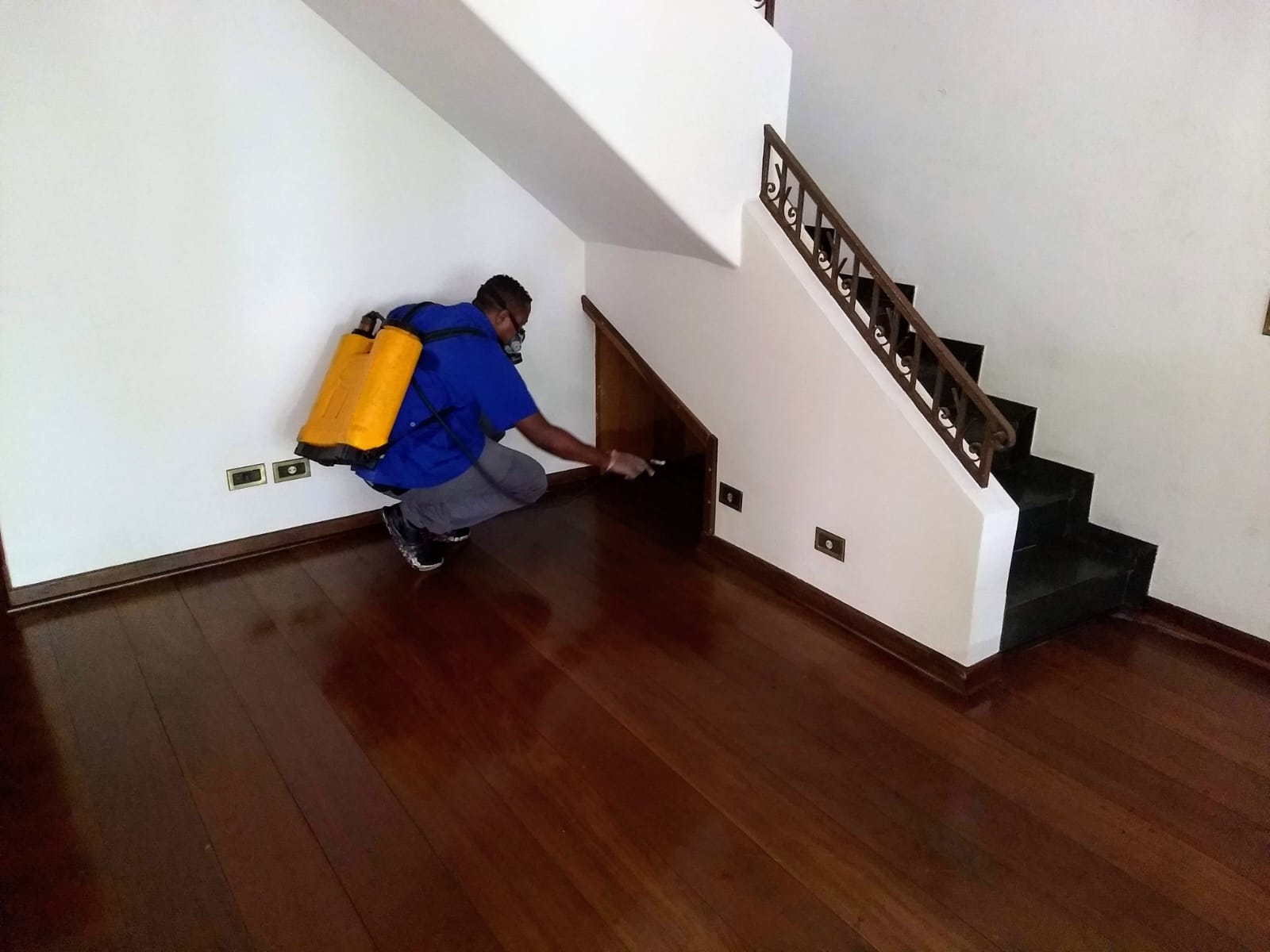 Técnico da GMs de camisa azul dedetizando sob a escada de uma residência em São Paulo