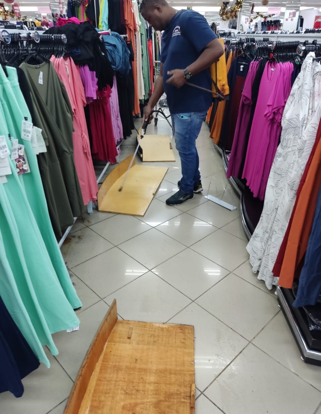 Técnico da GMs Controle de Pragas Urbanas aplicando produto no piso de uma loja de roupas, entre as araras